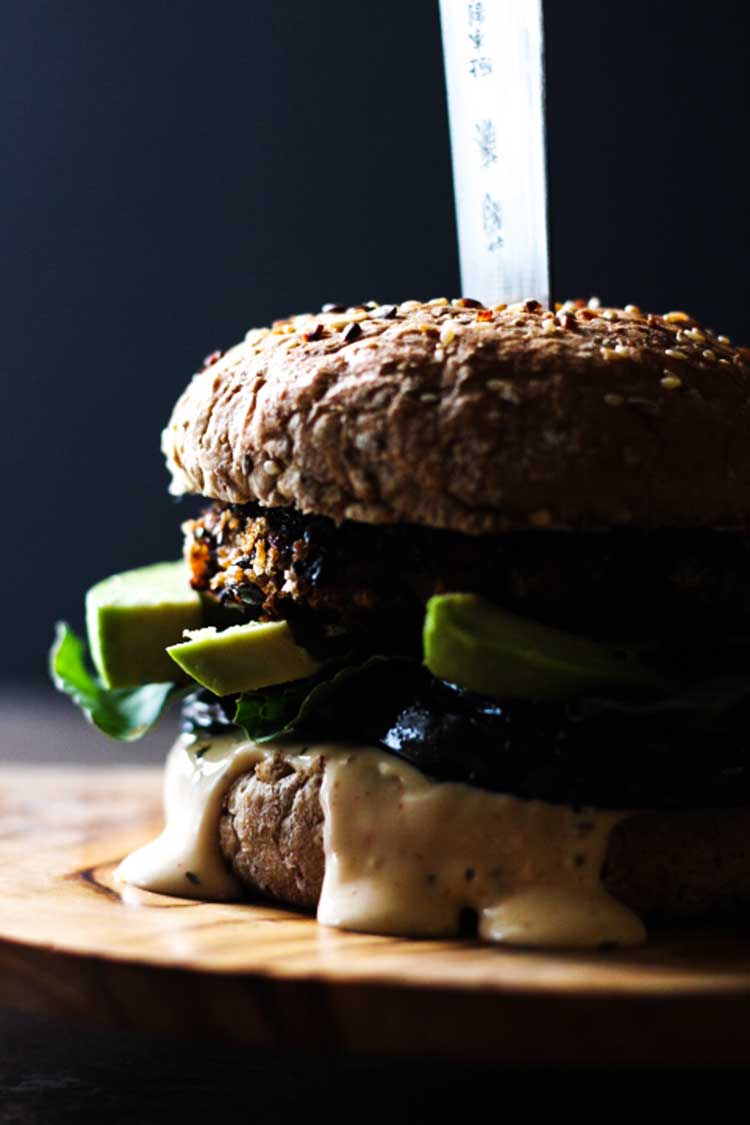 Close up side view of a black bean burger, assembled with avocado, mayo and rocket. 