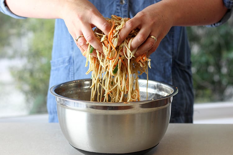 Soba noodle salad being tossed with the dressing. 