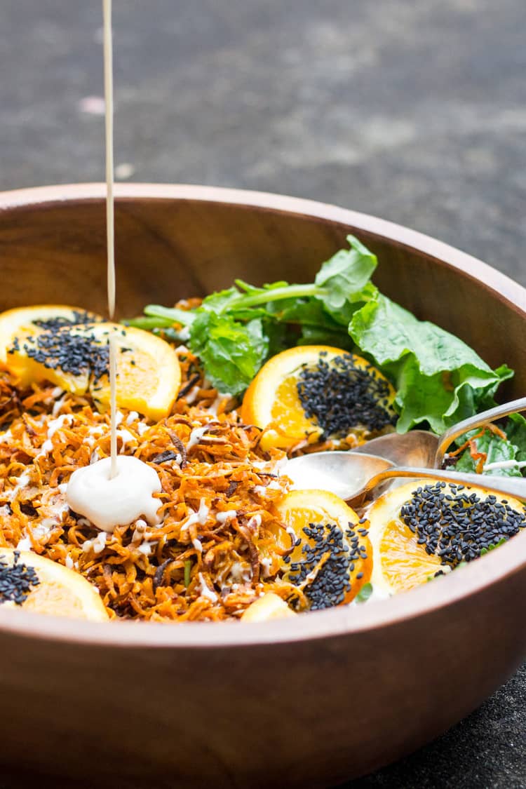 Pouring miso cashew dressing onto sweet potato and kale salad. 