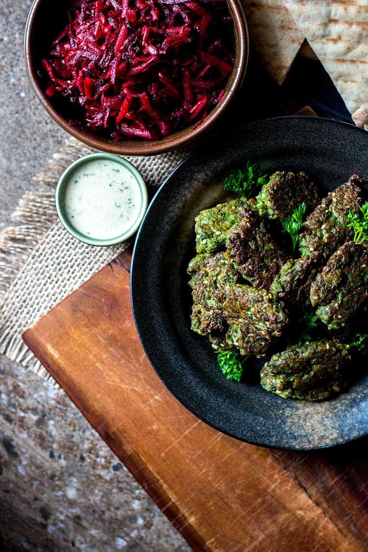 Overhead photo of broad bean falafel, tahini sauce and beetroot slaw, ready to serve with pita pockets.