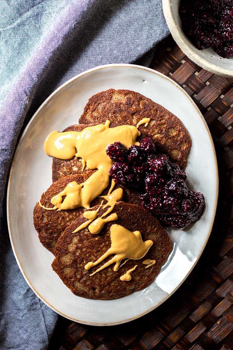Overhead shot of buckwheat pikelets, drizzled with peanut butter and a spoonful of blueberry chia jam (vegan and gluten free). 