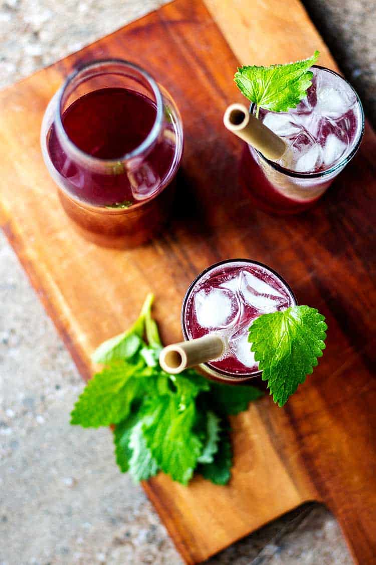 Overhead shot of boysenberry shrubs, mixed with soda water and garnished with a sprig of lemon balm. 