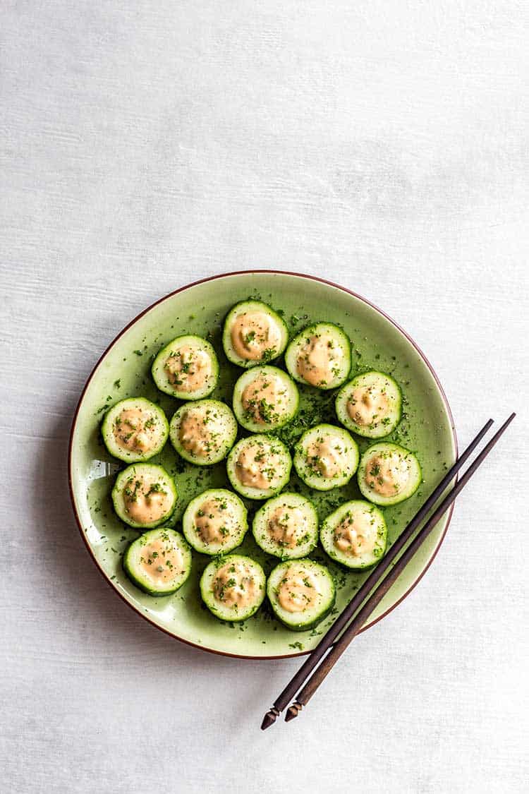 Overhead shot of cucumber sushi with white bean 'tuna' on a green plate. 