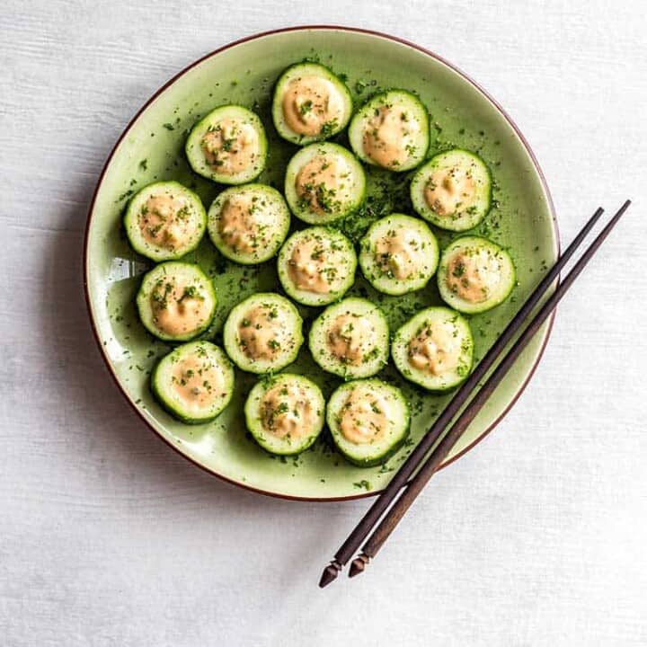 Overhead shot of cucumber sushi with white bean 'tuna' on a green plate.