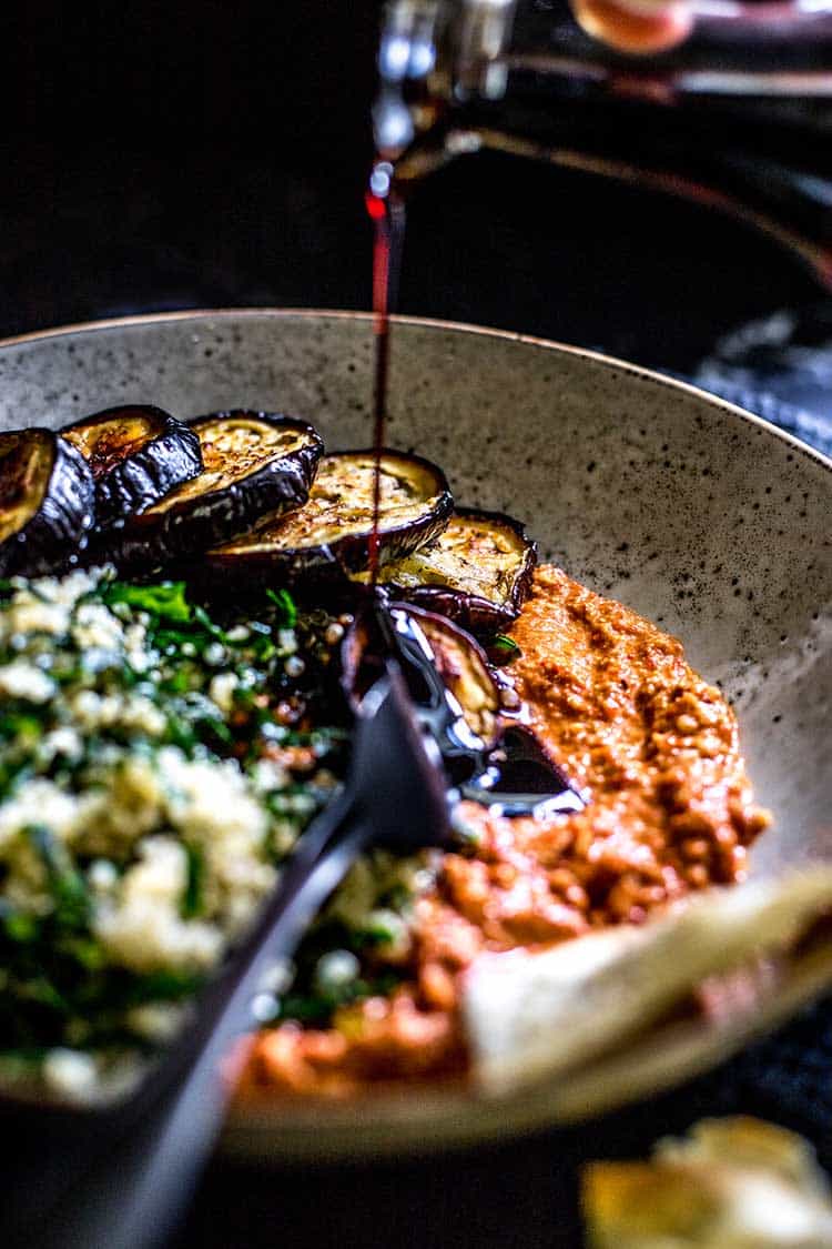 Quinoa, kale and eggplant bowl with muhammara dip. Pomegranate molasses being poured on to serve. 