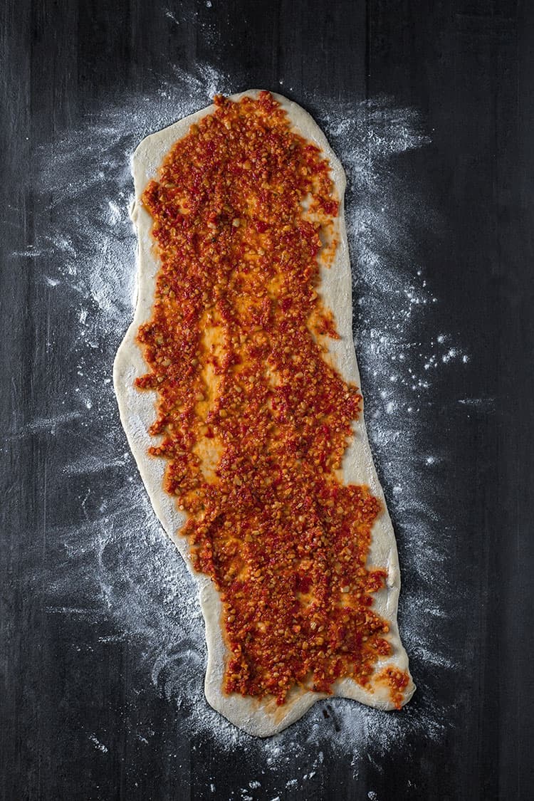 Bread dough rolled into a rectangle and smothered in red pesto.