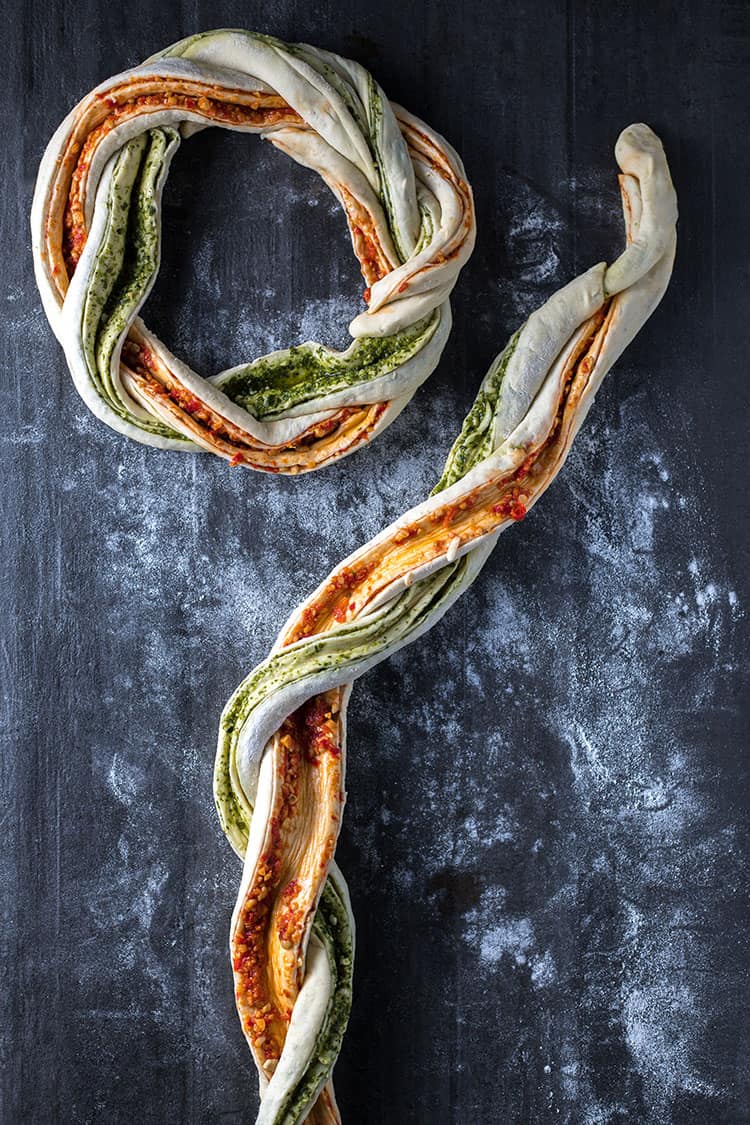 Snakes of pesto filled bread dough twisted together and formed into a bread wreath.