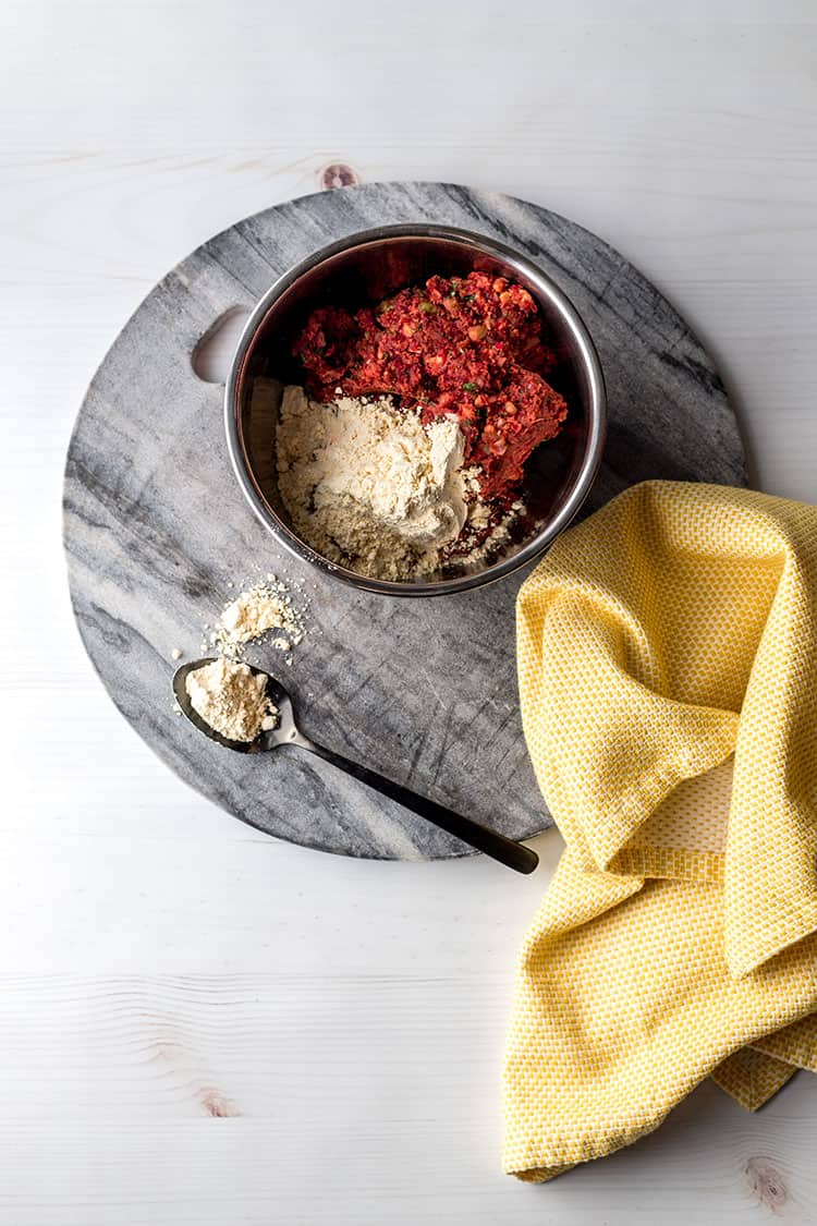 Home made beetroot falafel mixture in a mixing bowl, with chickpea flour being added. 