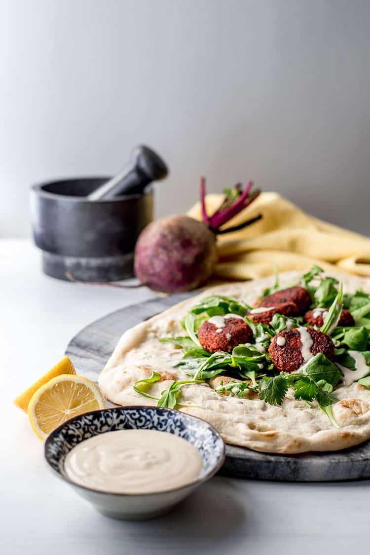 Beetroot falafel with tahini sauce (vegan and gluten free), pictured with salad greens and flat bread. 