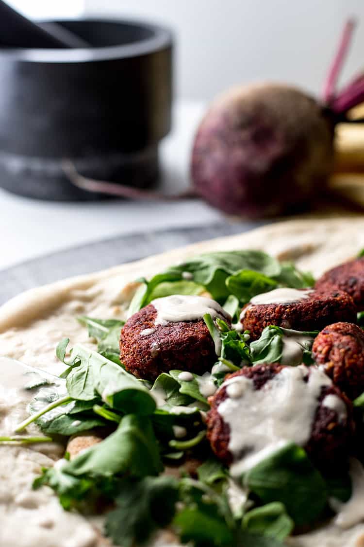 Close up photo of beetroot falafel drizzled with simple tahini sauce. 