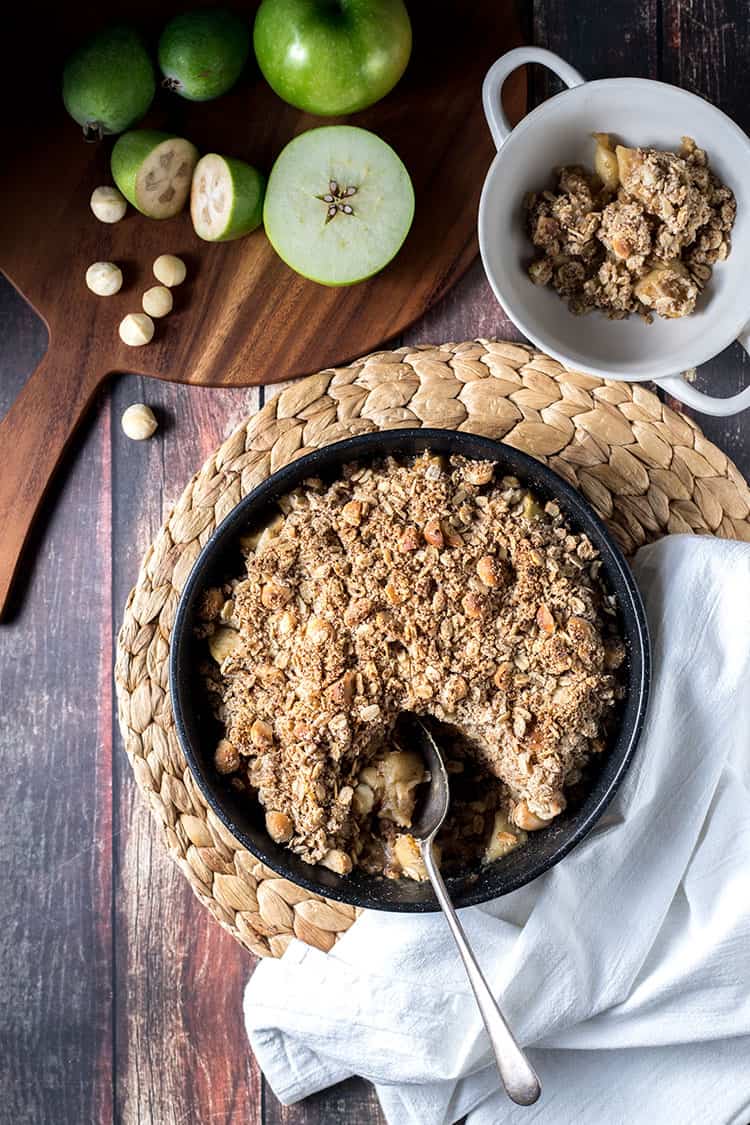 Apple and feijoa crumble with macadamias, pictured being served on a tabletop. 
