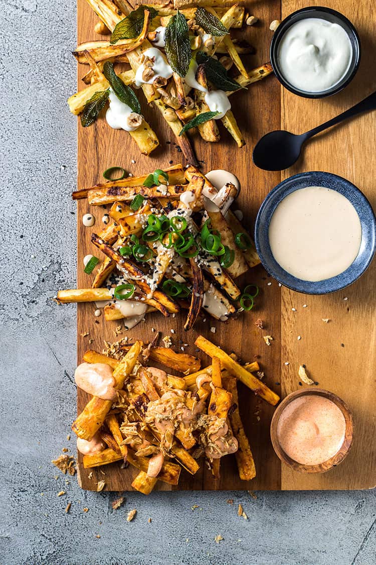 Three ways with roast parsnip and vegan aioli. Roasted parsnip on a chopping board with aioli dipping sauces and garnishes. 