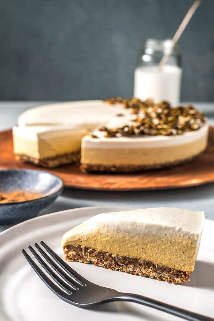 Vegan pumpkin pie cheesecake on a serving board with a slice removed and put on a serving plate. 