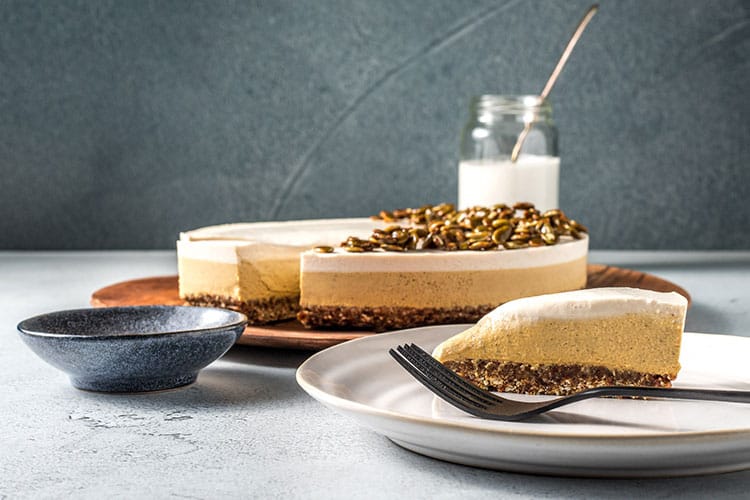 Vegan pumpkin pie chesecake on a serving board, with a slice removed to a serving plate. Gluten free. 