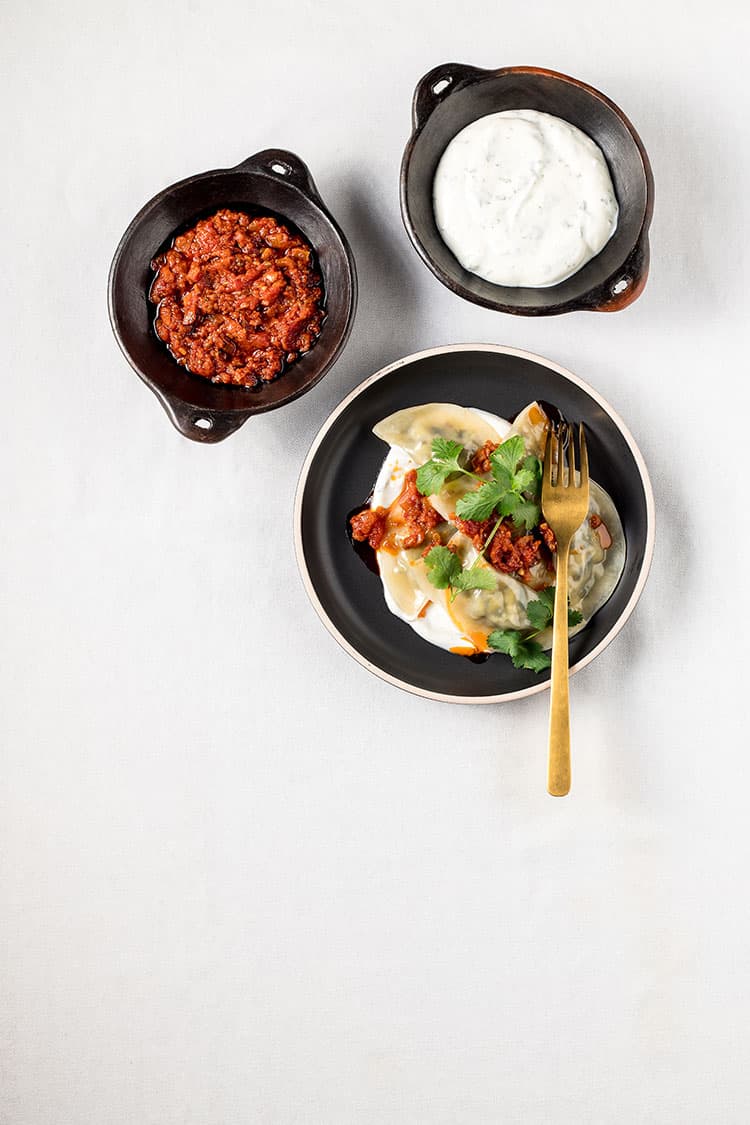 A plate of ashak - Afghan vegetable dumplings, served with minted garlic sauce and an oil-based tomato and garlic dressing.