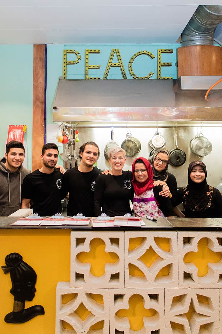 Tania Jones and the team at Home Kitchen, standing in a commercial kitchen under a sign saying 'Peace'.