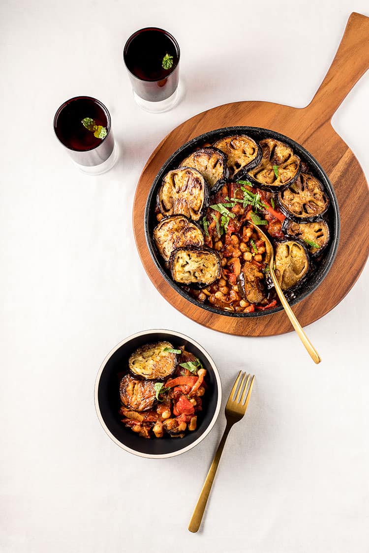 Maghmour - Lebanese eggplant and chickpea stew in a casserole dish, sitting on a wooden board ready to be served. 