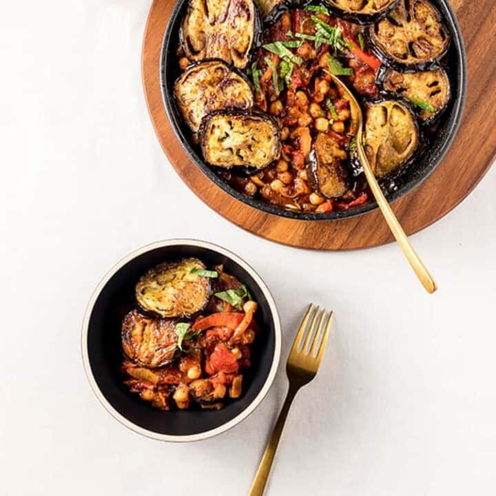 Maghmour - Lebanese eggplant and chickpea stew in a casserole dish, sitting on a wooden board ready to be served.