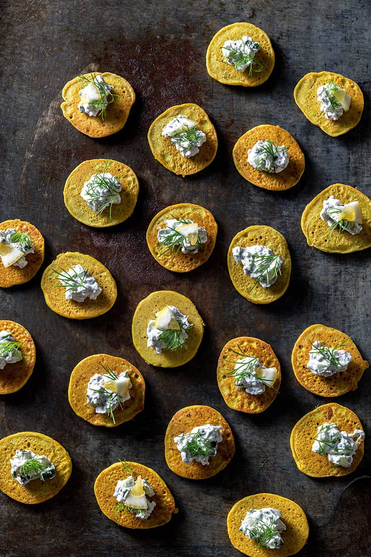 A baking tray with lots of vegan blini, topped with cucumber, fennel and yoghurt.