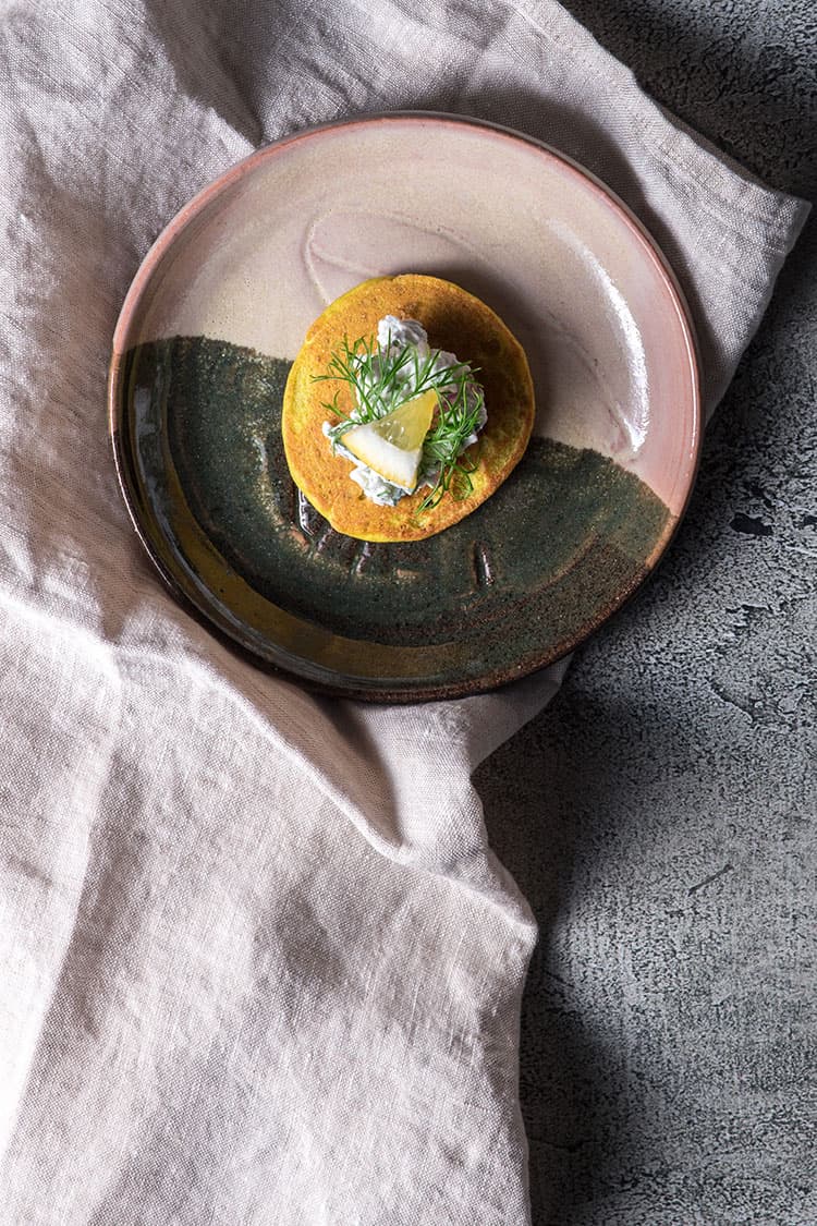 A single spiced vegan blini on a serving plate, sitting on top of a linen napkin. 
