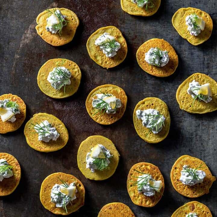 A baking tray with lots of vegan blini, topped with cucumber, fennel and yoghurt.