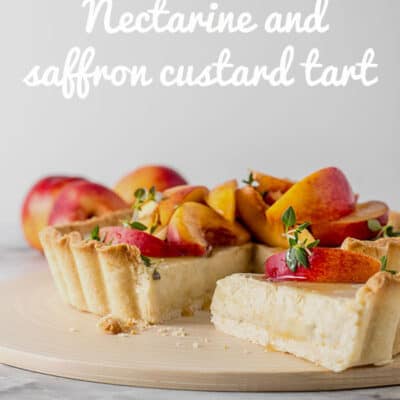 A vegan custard tart sitting on a chopping board, with a slice removed. The tart is topped with sliced nectarines, drizzled with honey and sprinkled with fresh thyme leaves.