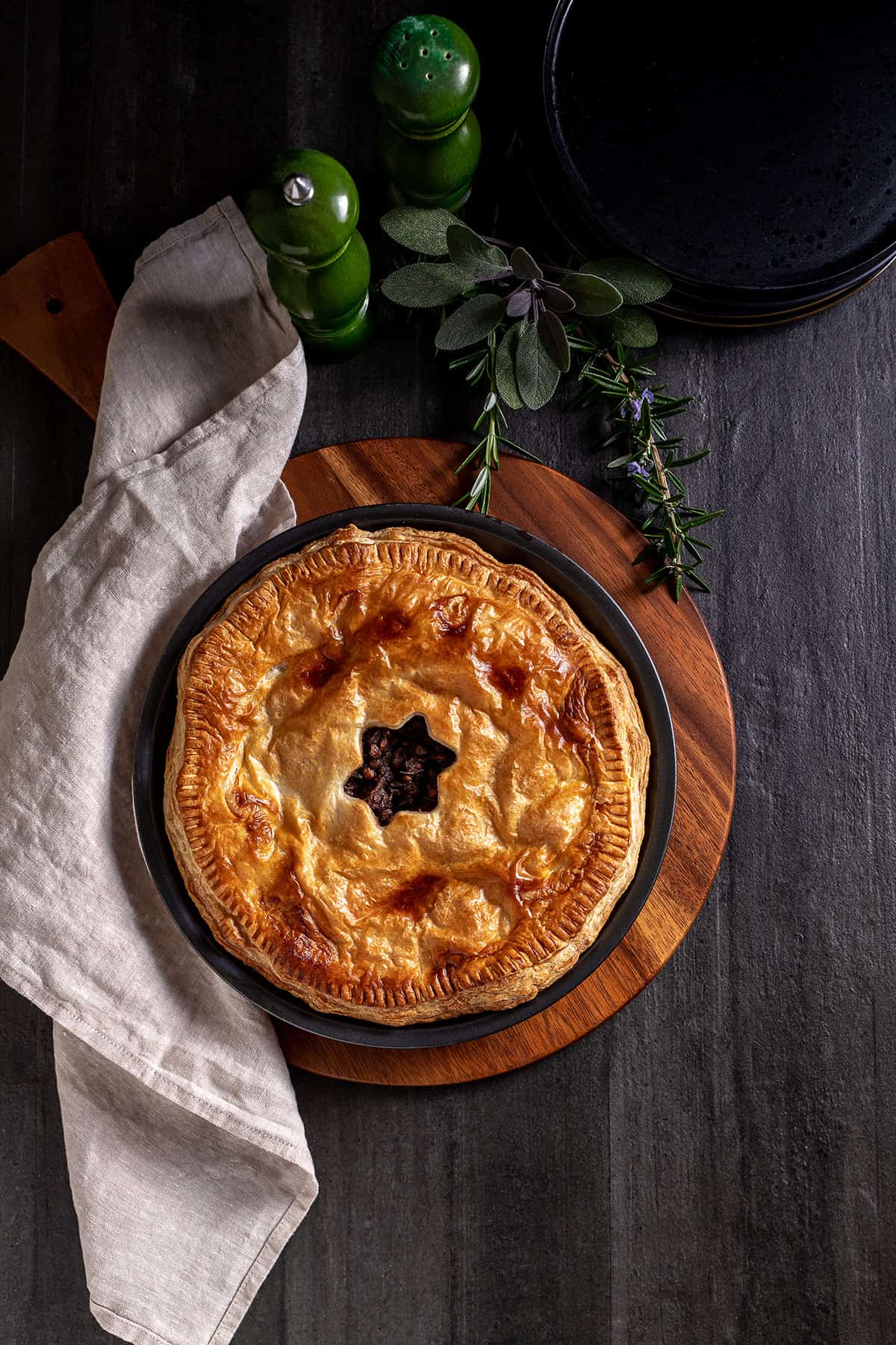 A cooked mushroom, onion and lentil pie in its pie tin, sitting on a chopping board. The pastry is golden brown, with a star shaped hole cut in the centre. 