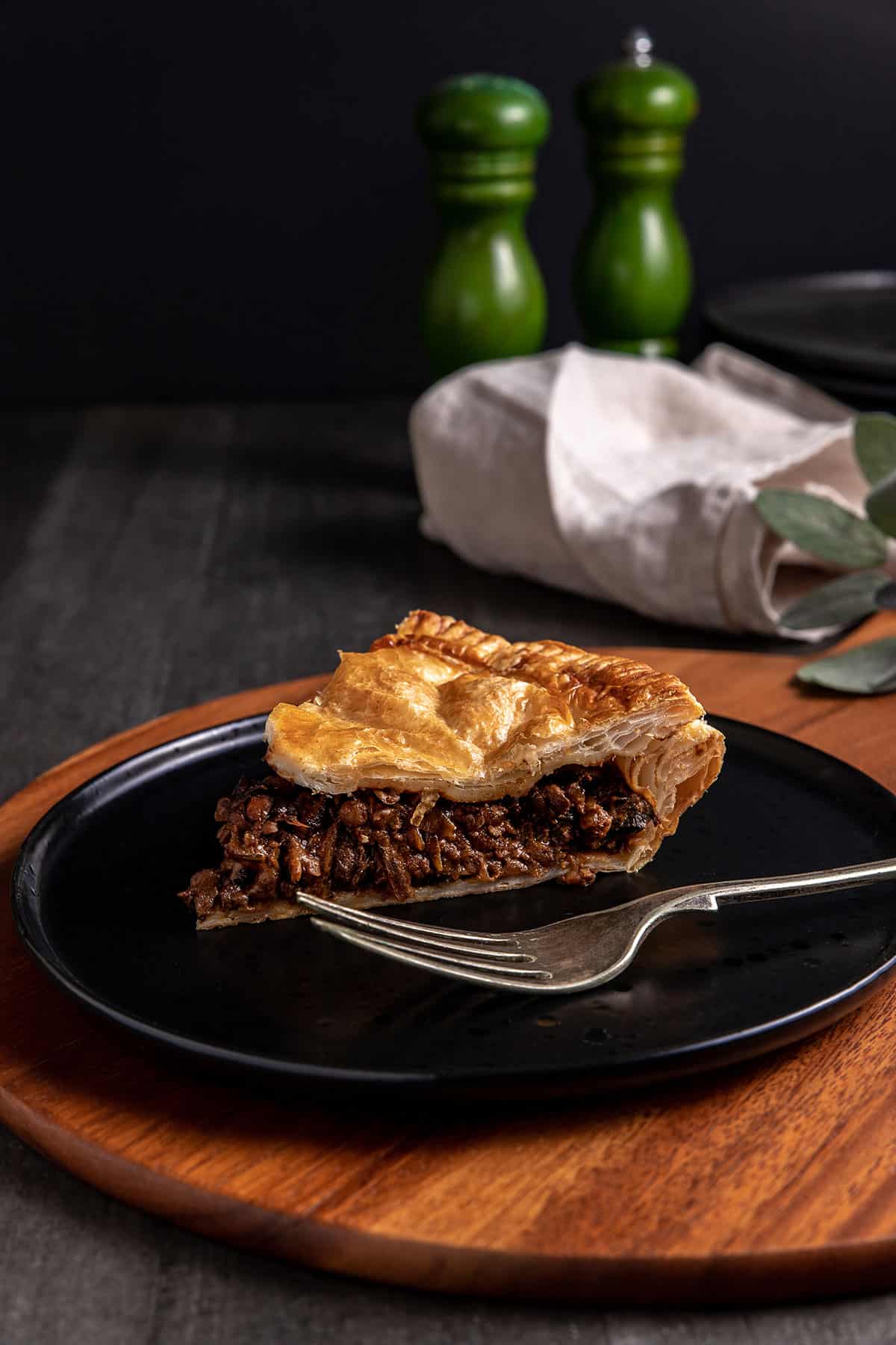 A slice of mushroom, onion and lentil pie sitting on a black plate. The filling is dark and glossy. 