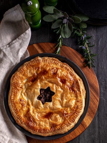 A cooked mushroom, onion and lentil pie in its pie tin, sitting on a chopping board. The pastry is golden brown, with a star shaped hole cut in the centre.