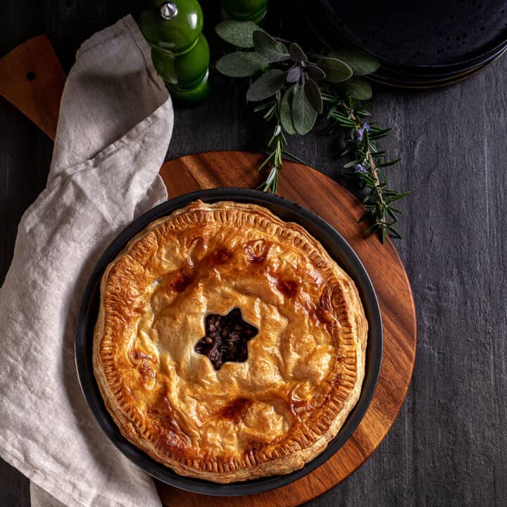 A cooked mushroom, onion and lentil pie in its pie tin, sitting on a chopping board. The pastry is golden brown, with a star shaped hole cut in the centre.