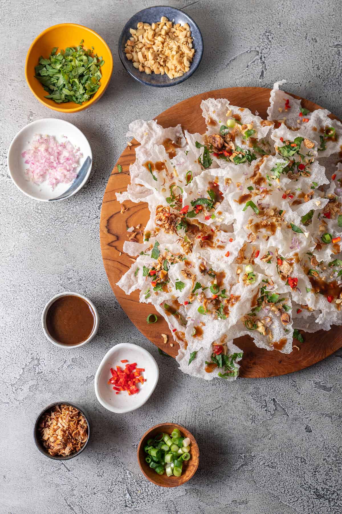 A wooden platter piled high with fried rice paper crisps, scattered with peanut, onion, coriander, shallots, spring onion and chilli. 