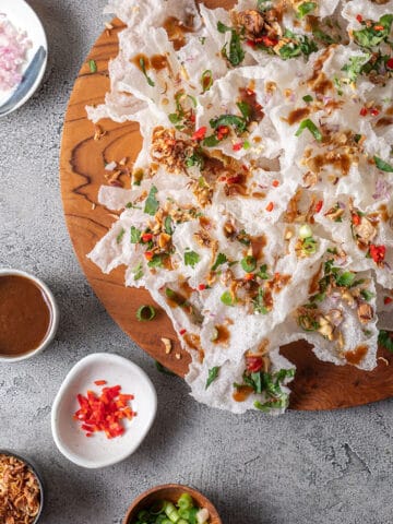 A wooden platter piled high with fried rice paper crisps, scattered with peanut, onion, coriander, shallots, spring onion and chilli.