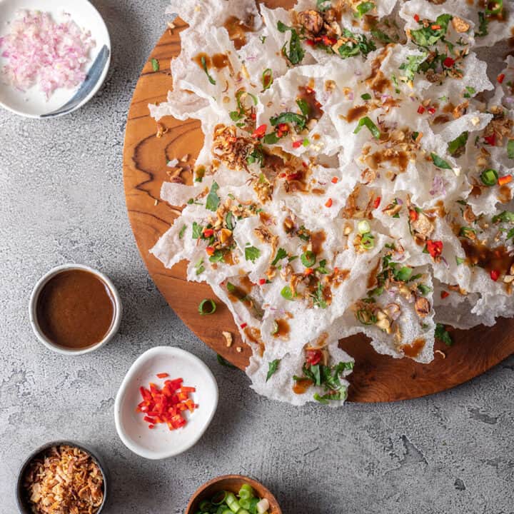 A wooden platter piled high with fried rice paper crisps, scattered with peanut, onion, coriander, shallots, spring onion and chilli.