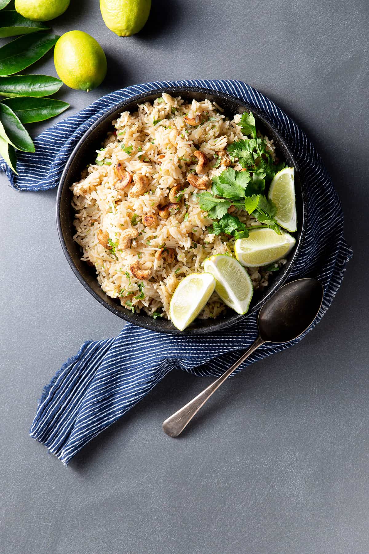 A black bowl containing rice pilaf, with cashew nuts, coriander (cilantro) and lime segments visible.