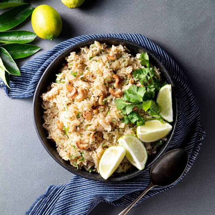 A black bowl containing rice pilaf, with cashew nuts, coriander (cilantro) and lime segments visible.