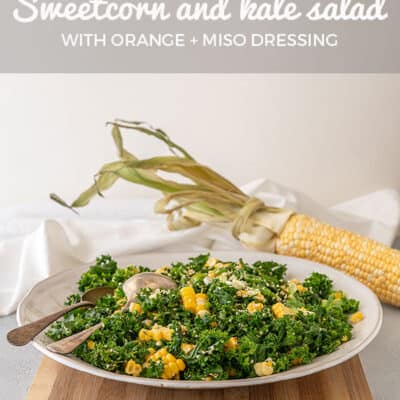 A wide white bowl with sweetcorn and kale salad in it, sitting on a bamboo chopping board. A whole cob of corn is in the background.