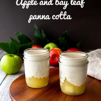 Two vegan panna cotta desserts served in glass jars, sitting on a wooden board, with apples and bay leaves in the background.