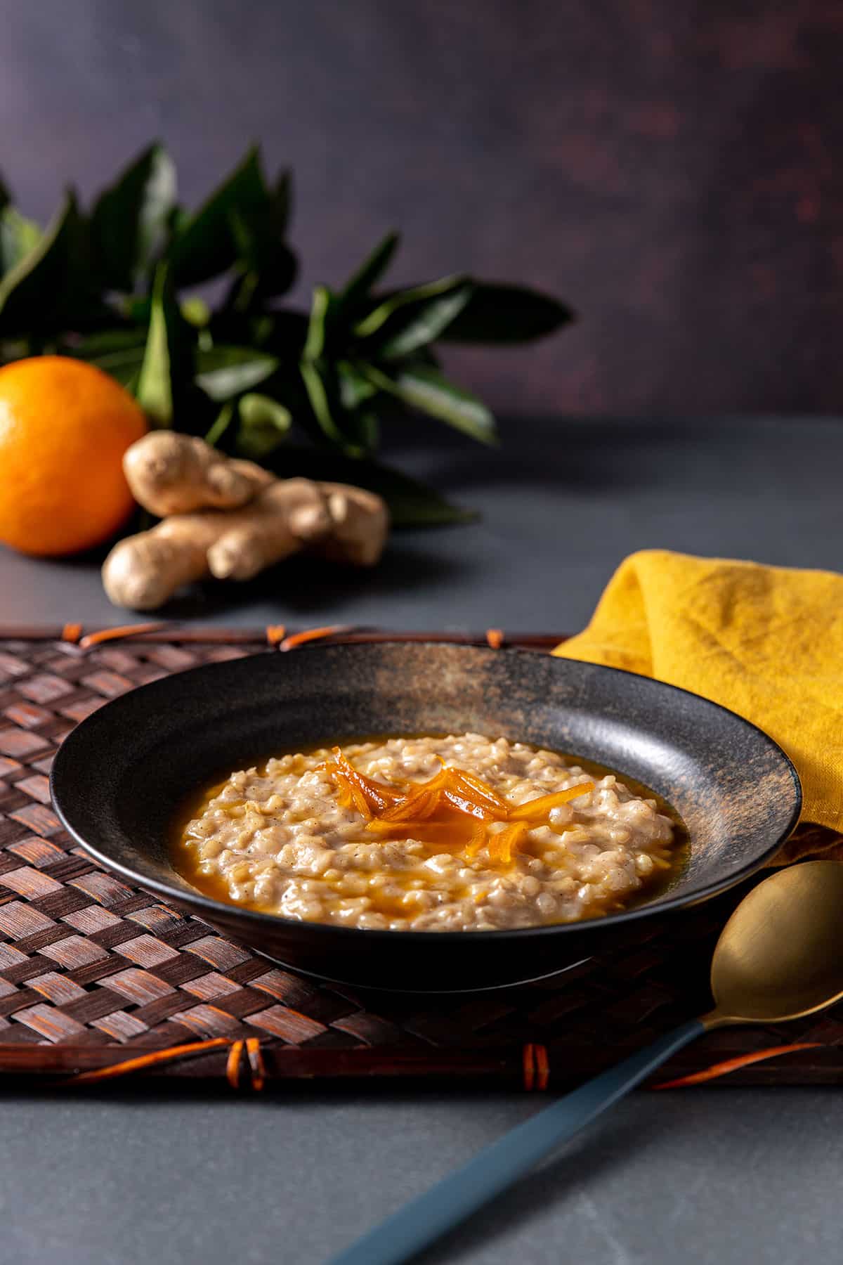 A pottery bowl holds creamy brown rice pudding, topped with an orange syrup and strips of orange zest. 