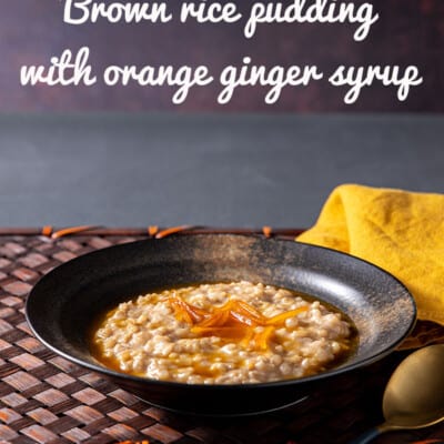 A pottery bowl holds creamy brown rice pudding, topped with an orange syrup and strips of orange zest.
