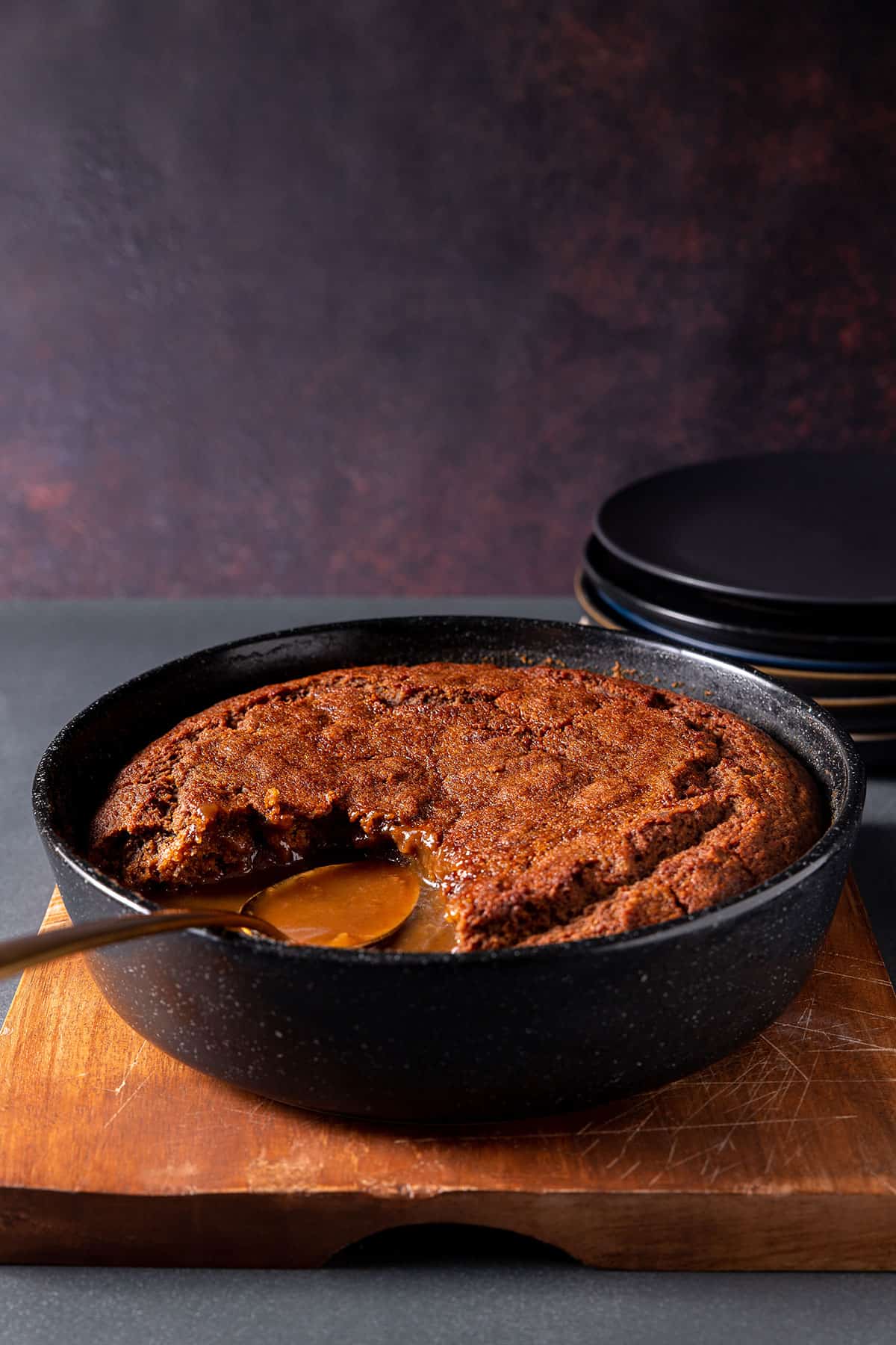A dish of self saucing pudding, with a serving removed, showing the glossy sauce. 