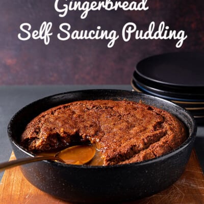 A casserole dish of gingerbread self saucing pudding, with a serving removed to reveal the luscious, shiny sauce below.