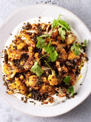 A white plate smeared with yoghurt, topped with cauliflower that has been tossed in harissa paste and roasted, and a scattering of crunchy fried green lentils.n